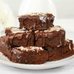 Decadent chocolate brownies with a hint of cannabis, sitting on a white plate with a drizzle of chocolate ganache and a sprinkling of powdered sugar.