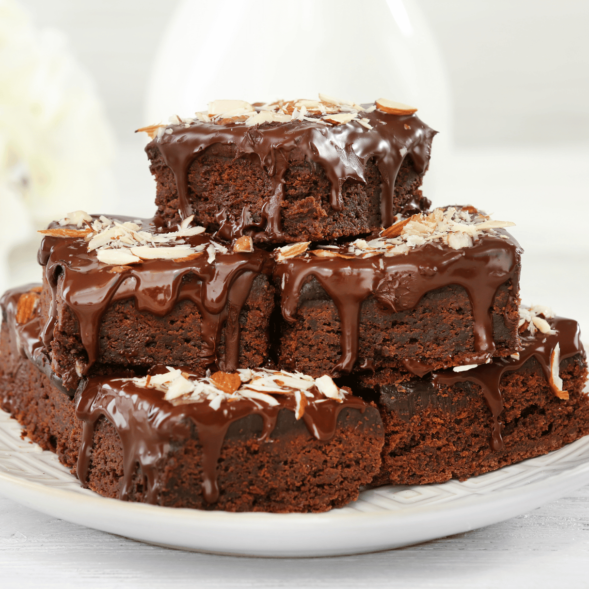 Decadent chocolate brownies with a hint of cannabis, sitting on a white plate with a drizzle of chocolate ganache and a sprinkling of powdered sugar.