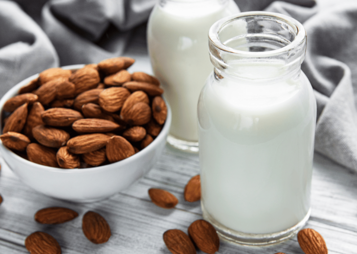 A glass bottle filled with creamy homemade infused almond milk, with scattered almonds in the background
