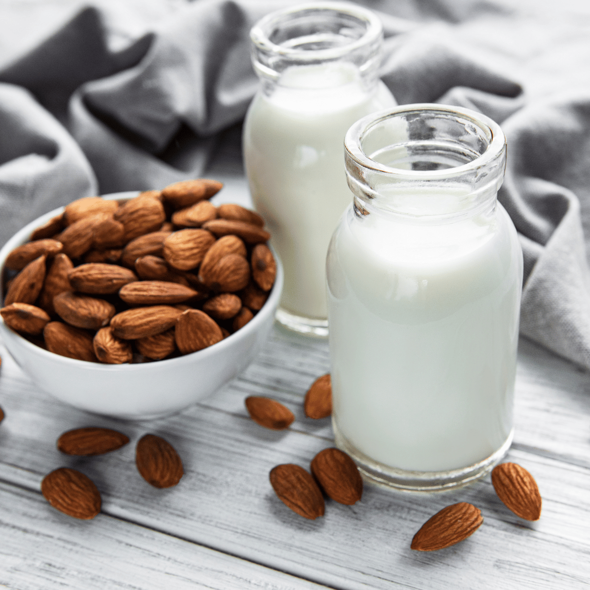 A glass bottle filled with creamy homemade infused almond milk, with scattered almonds in the background